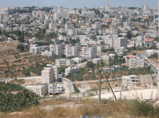 View of Ramallah from Beit-El, with the buffers between the two. The first building with the red roof on the right hand side of the photo next to a parking lot with cars is the PA Ministry of Health.
