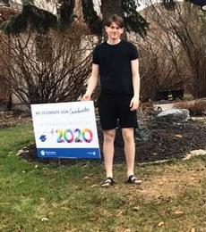 A grade 12 graduate beside his lawn sign